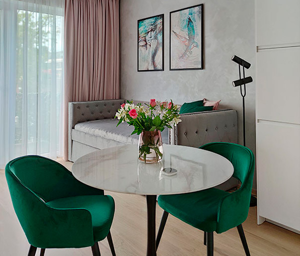 Современная небольшая квартира с круглым обеденным столом, зелеными бархатными стульями и светло-серым диваном, предназначенная для краткосрочной аренды в Праге.